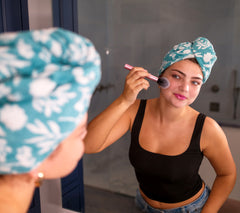 Picture of a women brushing her face while wearing a 100% Cotton Turbie Twist in the color Aqua with a White Floral Pattern.