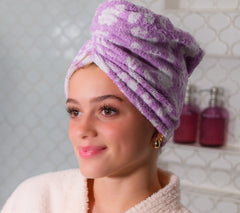 Picture of a women wearing a 100% Cotton Turbie Twist in the color Purple with a White Floral Pattern.