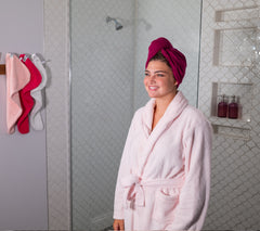 Photo of a women wearing a 100% Cotton Turbie Twist in the color Deep Raspberry. With the colors Bright Raspberry, Strawberry, and White hanging on the wall
