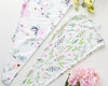 Two microfiber hair towels laying on a white surface next to flowers. The towels have botanical prints.