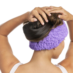 Photo of a woman, facing the back, wearing a purple Turbie band, with her hands on her head, holding her hair.