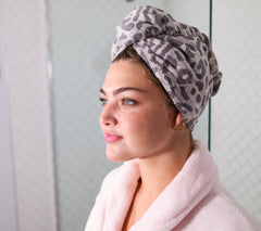 Photo of woman in a bathroom wearing a grey leopard print 100% cotton Turbie Twist Hair Towel.