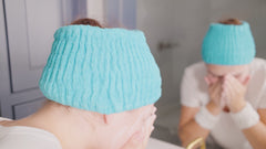 Relaxed self-care moment featuring a woman in a spa-like setting wearing the Turbie Band by Turbie Twist, an extra wide & stretchy headband made of 100% Cotton.  The woman is demonstrating its ease of use, comfort & functionality for use  for face washing, skincare and general lifestyle.